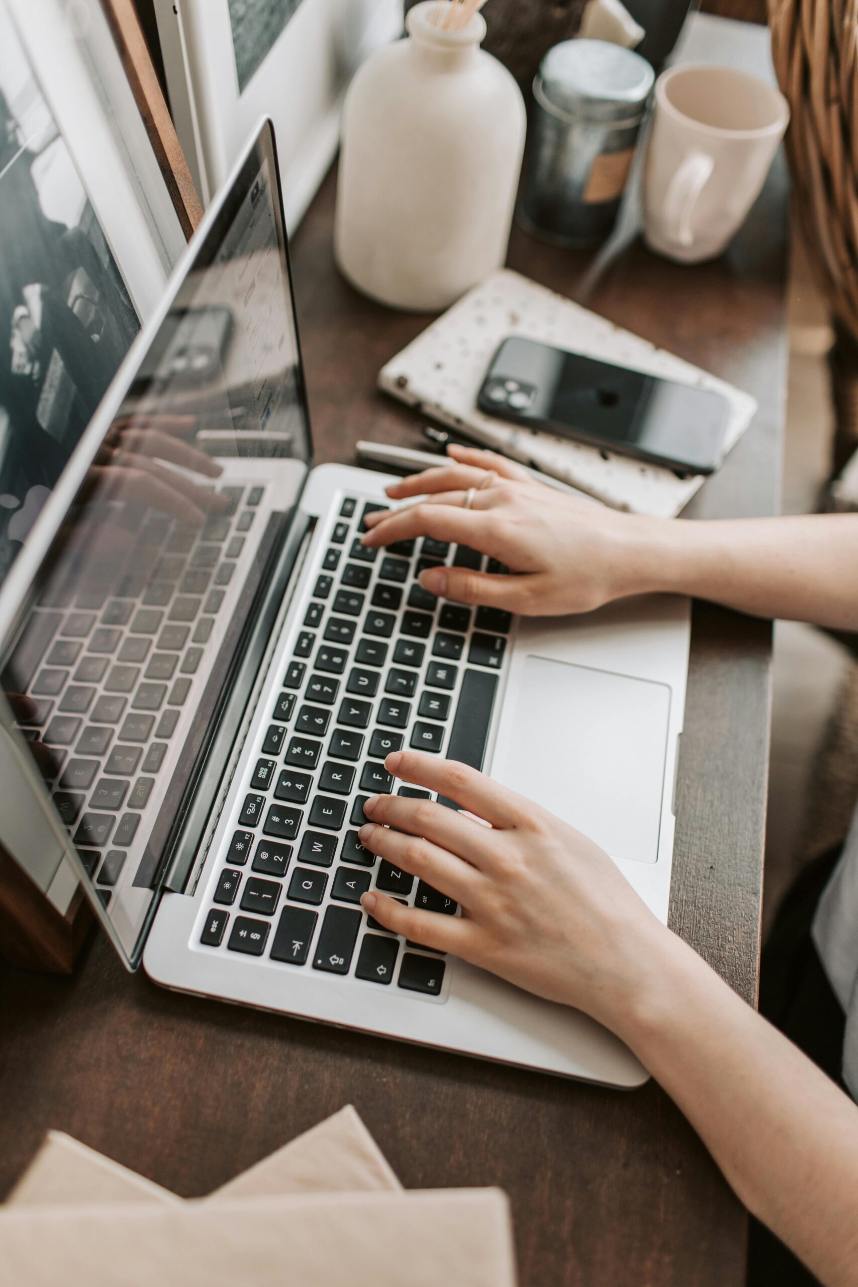 From above of unrecognizable woman sitting at table and typing on keyboard of computer during remote work in modern workspace